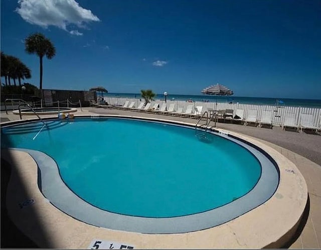 view of swimming pool with a patio area, a water view, and a view of the beach