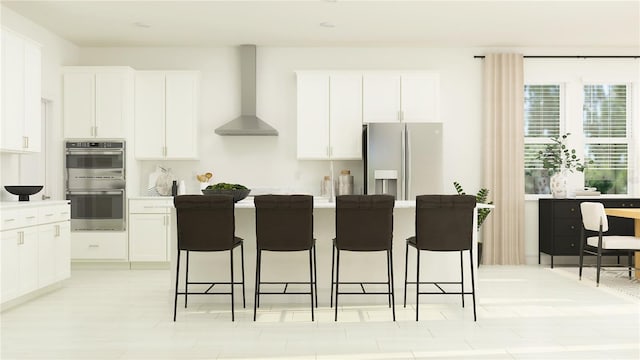 kitchen with a kitchen bar, stainless steel appliances, white cabinetry, and wall chimney range hood