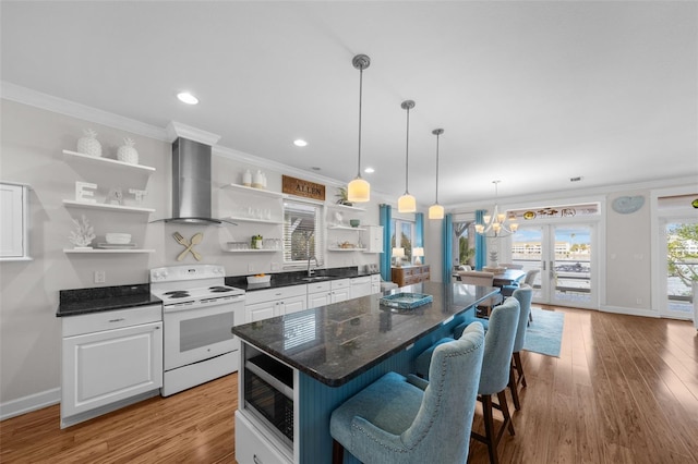 kitchen featuring wall chimney range hood, crown molding, built in microwave, white range with electric stovetop, and white cabinetry