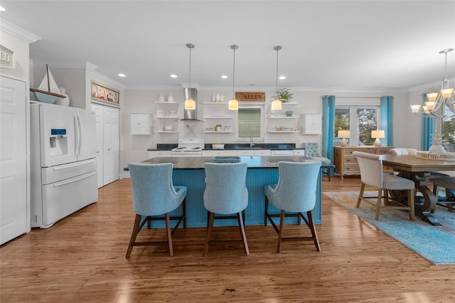 kitchen featuring white appliances, hanging light fixtures, a notable chandelier, and wall chimney range hood