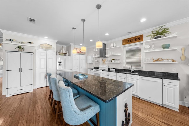 kitchen featuring wall chimney exhaust hood, white appliances, sink, a center island, and white cabinetry