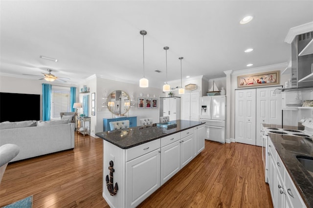 kitchen with white refrigerator with ice dispenser, decorative light fixtures, range, a center island, and white cabinetry