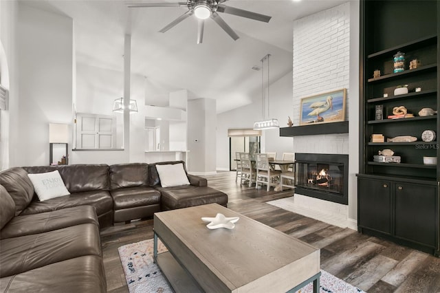 living room featuring dark hardwood / wood-style flooring, built in shelves, ceiling fan, high vaulted ceiling, and a fireplace