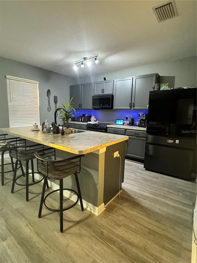 kitchen featuring a breakfast bar area, gray cabinets, light hardwood / wood-style flooring, and black appliances