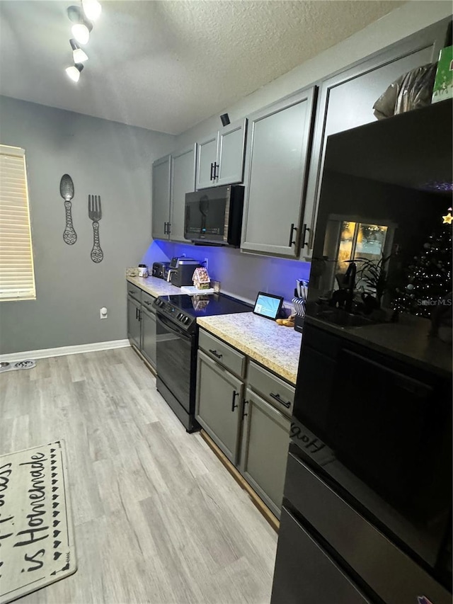 kitchen featuring black appliances, gray cabinetry, a textured ceiling, and light hardwood / wood-style flooring