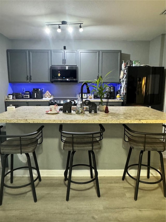 kitchen featuring a kitchen breakfast bar, gray cabinets, black fridge, and light hardwood / wood-style flooring