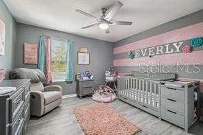 bedroom with light hardwood / wood-style floors, a nursery area, and ceiling fan