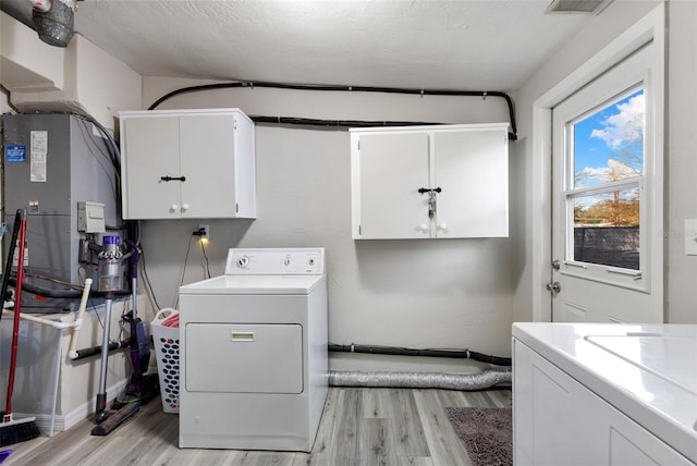 clothes washing area featuring washing machine and dryer, cabinets, a textured ceiling, and light wood-type flooring