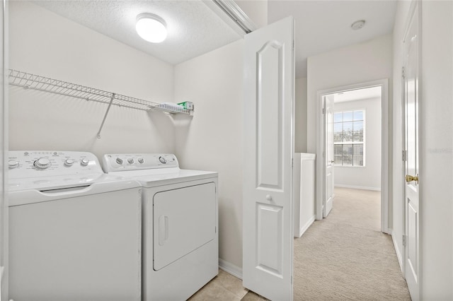 laundry area featuring washer and clothes dryer, light colored carpet, and a textured ceiling