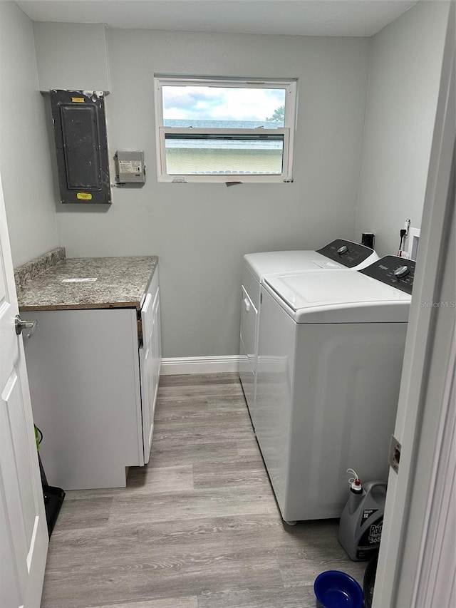 clothes washing area featuring washer and clothes dryer, cabinets, light wood-type flooring, and electric panel