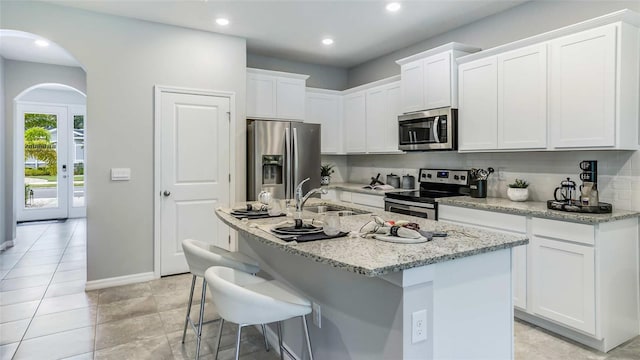 kitchen featuring light stone countertops, sink, stainless steel appliances, a center island with sink, and white cabinets