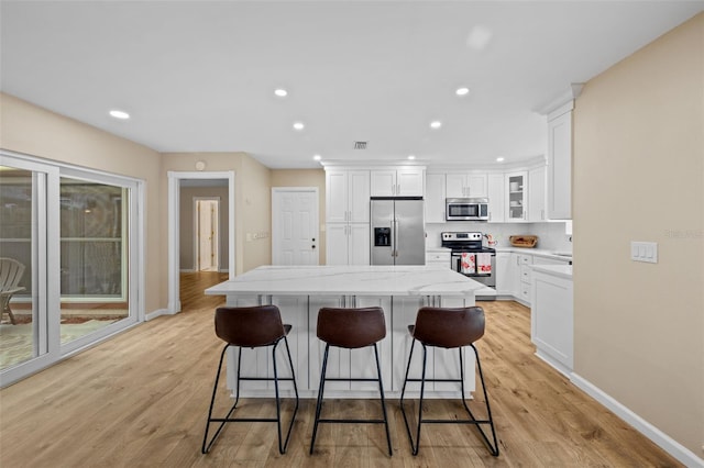 kitchen featuring a kitchen island, white cabinetry, a breakfast bar area, light hardwood / wood-style floors, and stainless steel appliances