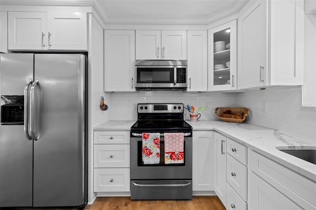 kitchen with tasteful backsplash, light stone counters, light wood-type flooring, appliances with stainless steel finishes, and white cabinets