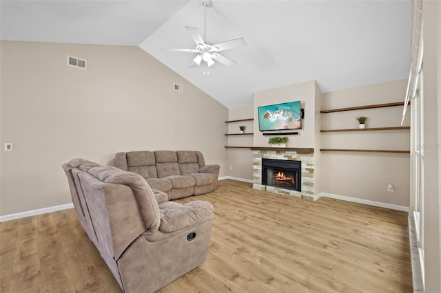 living room with lofted ceiling, a stone fireplace, ceiling fan, and light wood-type flooring