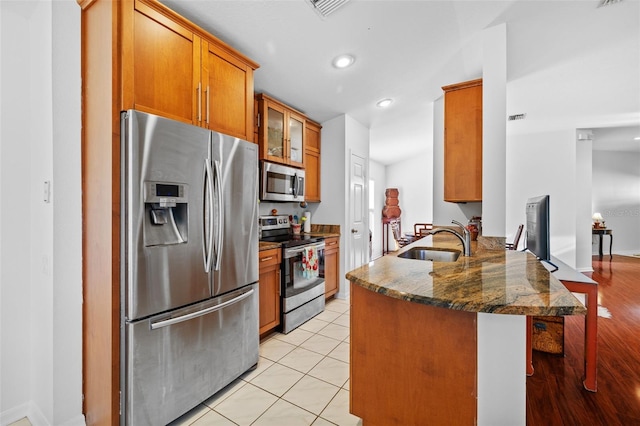 kitchen featuring kitchen peninsula, appliances with stainless steel finishes, dark stone counters, sink, and light tile patterned floors