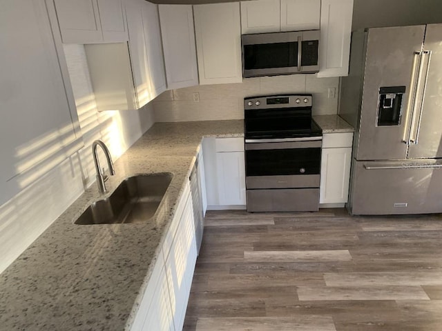 kitchen with appliances with stainless steel finishes, light stone counters, sink, light hardwood / wood-style flooring, and white cabinetry