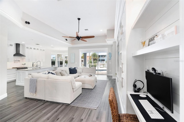 living room with a raised ceiling, ceiling fan, sink, and light hardwood / wood-style floors