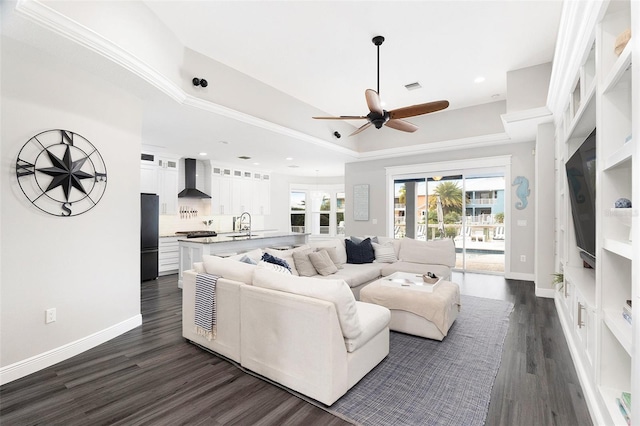 living room featuring ceiling fan, sink, dark wood-type flooring, a raised ceiling, and ornamental molding