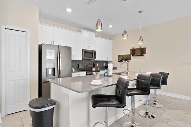 kitchen with white cabinets, hanging light fixtures, stainless steel appliances, and a kitchen island with sink