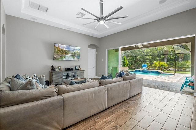 living room featuring ceiling fan, a healthy amount of sunlight, a raised ceiling, and ornamental molding