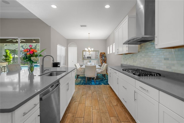 kitchen with white cabinets, wall chimney range hood, sink, decorative light fixtures, and stainless steel appliances