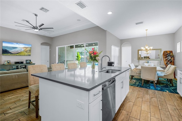 kitchen featuring stainless steel dishwasher, sink, white cabinets, hanging light fixtures, and an island with sink