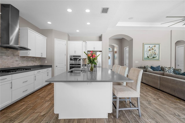 kitchen featuring white cabinetry, a center island with sink, wall chimney range hood, and appliances with stainless steel finishes