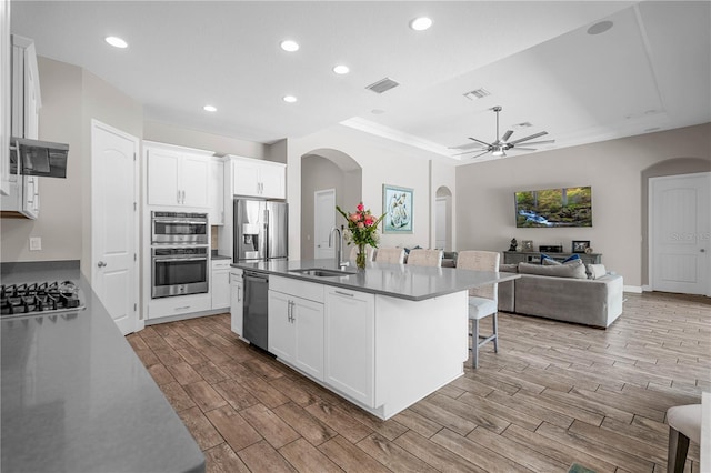 kitchen with appliances with stainless steel finishes, ceiling fan, a kitchen island with sink, sink, and white cabinetry