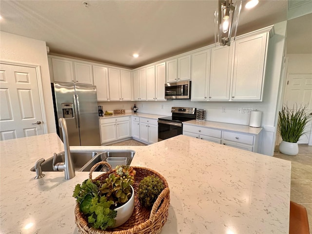 kitchen with white cabinetry, sink, light stone counters, pendant lighting, and appliances with stainless steel finishes