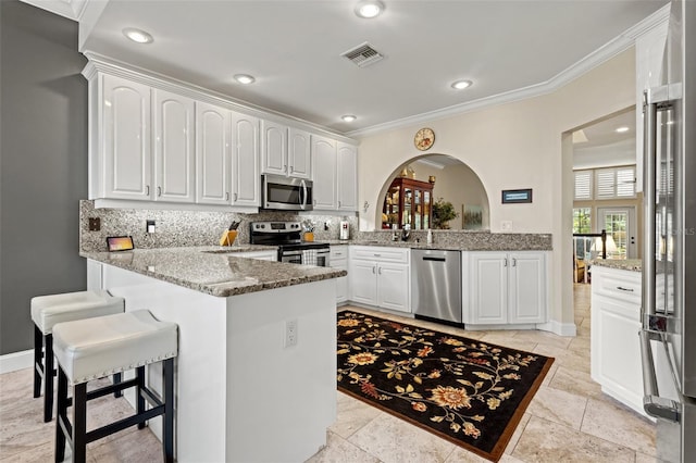 kitchen with kitchen peninsula, appliances with stainless steel finishes, tasteful backsplash, light stone counters, and white cabinetry