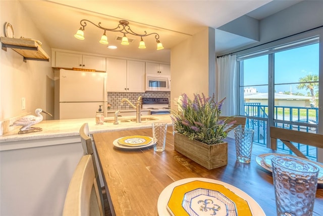 kitchen with white appliances, backsplash, sink, light stone counters, and white cabinetry