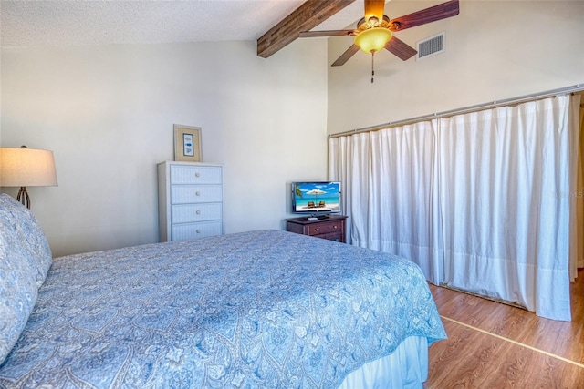 bedroom with ceiling fan, lofted ceiling with beams, a textured ceiling, and hardwood / wood-style flooring