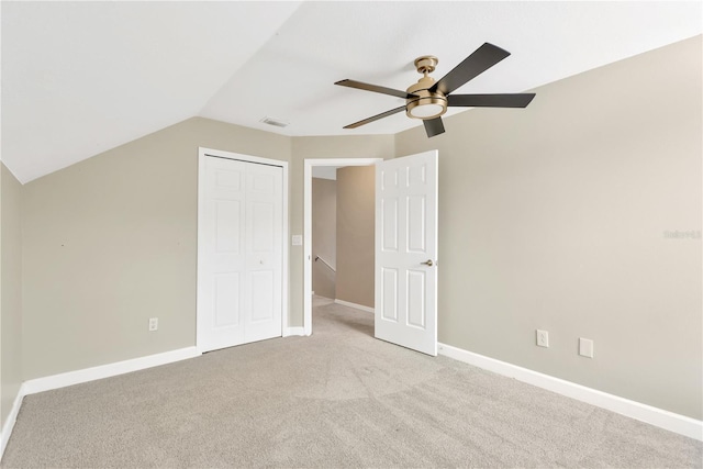 unfurnished bedroom featuring ceiling fan, a closet, light colored carpet, and vaulted ceiling