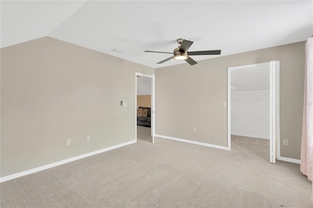 unfurnished bedroom featuring light carpet, a walk in closet, ceiling fan, a closet, and lofted ceiling