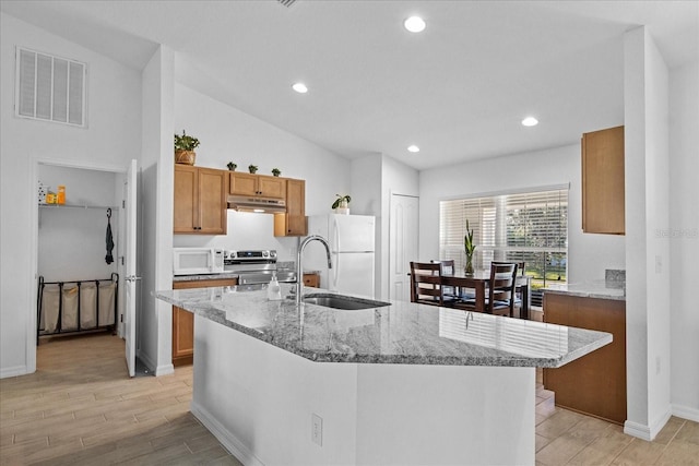 kitchen featuring lofted ceiling, sink, white appliances, a kitchen island with sink, and light stone countertops