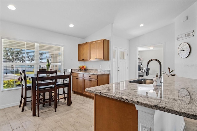 kitchen featuring light hardwood / wood-style floors, kitchen peninsula, vaulted ceiling, light stone counters, and sink