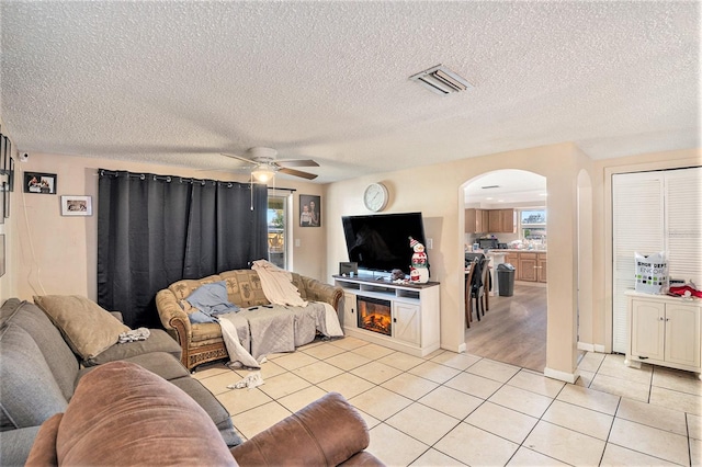 tiled living room featuring ceiling fan, a fireplace, a textured ceiling, and a wealth of natural light