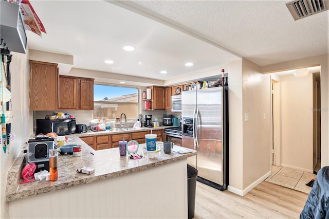 kitchen with kitchen peninsula, stainless steel refrigerator with ice dispenser, light stone counters, sink, and light hardwood / wood-style flooring