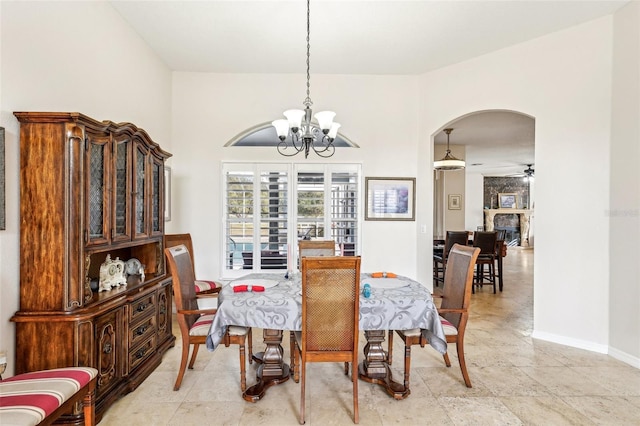 dining area featuring ceiling fan with notable chandelier and a stone fireplace