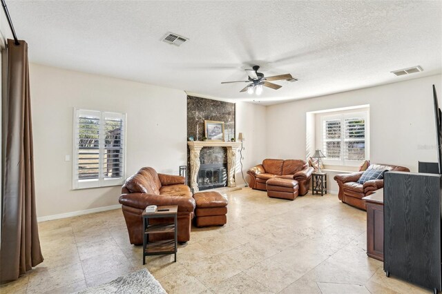 living room featuring plenty of natural light, ceiling fan, a stone fireplace, and a textured ceiling