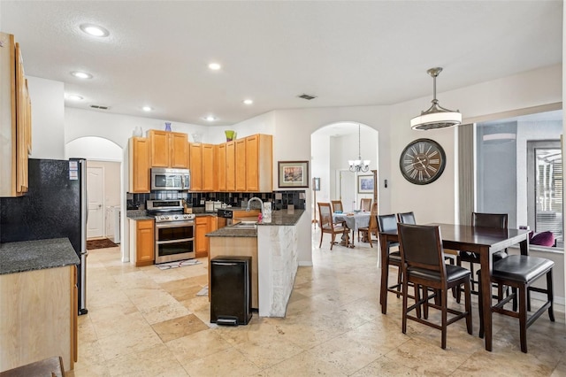 kitchen with kitchen peninsula, backsplash, stainless steel appliances, sink, and pendant lighting