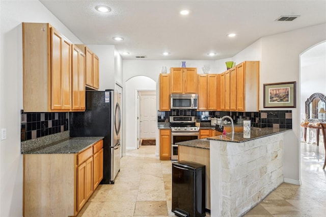 kitchen featuring sink, tasteful backsplash, dark stone countertops, kitchen peninsula, and appliances with stainless steel finishes