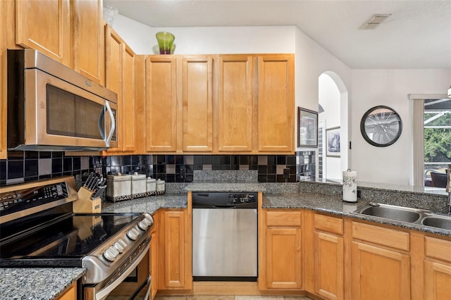 kitchen with tasteful backsplash, dark stone countertops, sink, and appliances with stainless steel finishes