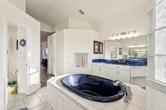 bathroom with tile patterned floors, vanity, a relaxing tiled tub, and vaulted ceiling