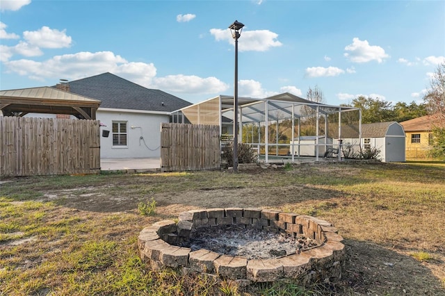 view of yard featuring an outdoor fire pit, glass enclosure, a storage unit, and a patio area