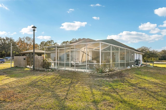 rear view of house featuring a lanai, central air condition unit, and a yard