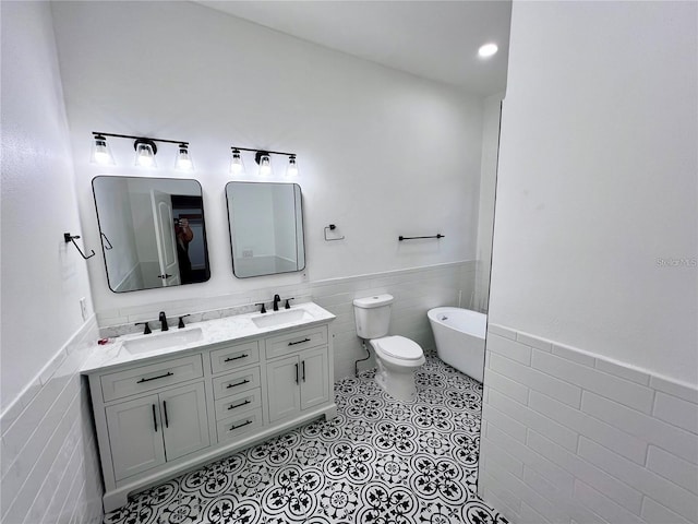 bathroom with a bath, tile patterned floors, toilet, vanity, and tile walls