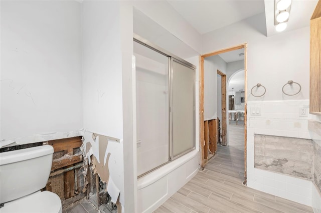 bathroom featuring toilet and bath / shower combo with glass door