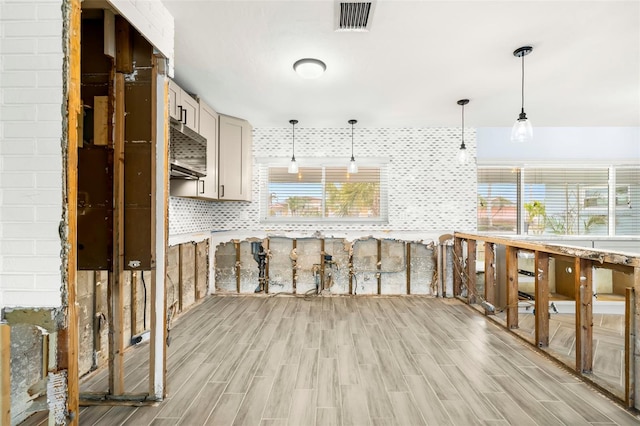 kitchen with a wealth of natural light, pendant lighting, light wood-type flooring, and decorative backsplash