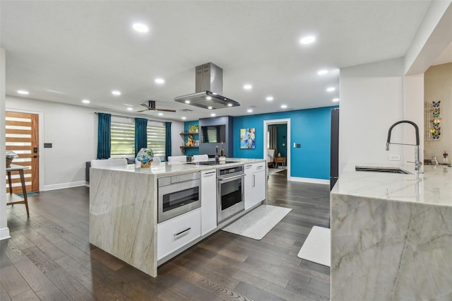 kitchen with oven, sink, light stone countertops, and an island with sink